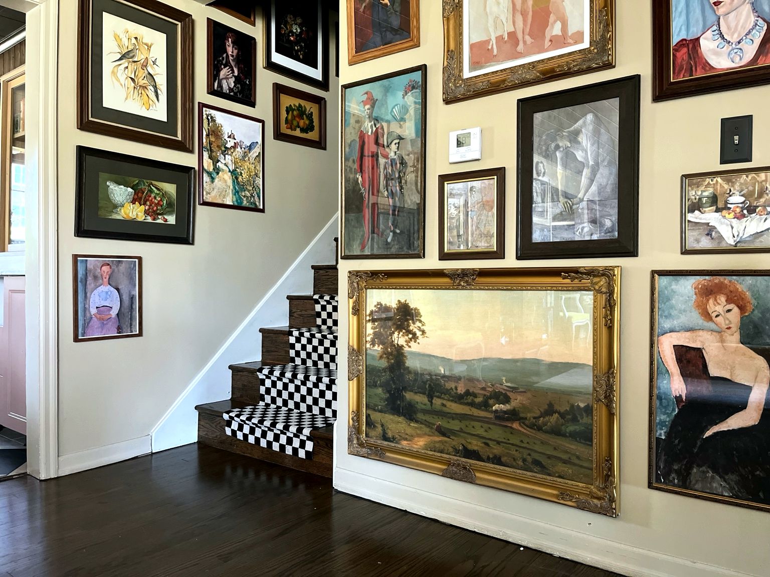 Gallery wall of antique portraits and landscapes in gilded frames beside a checkerboard staircase
